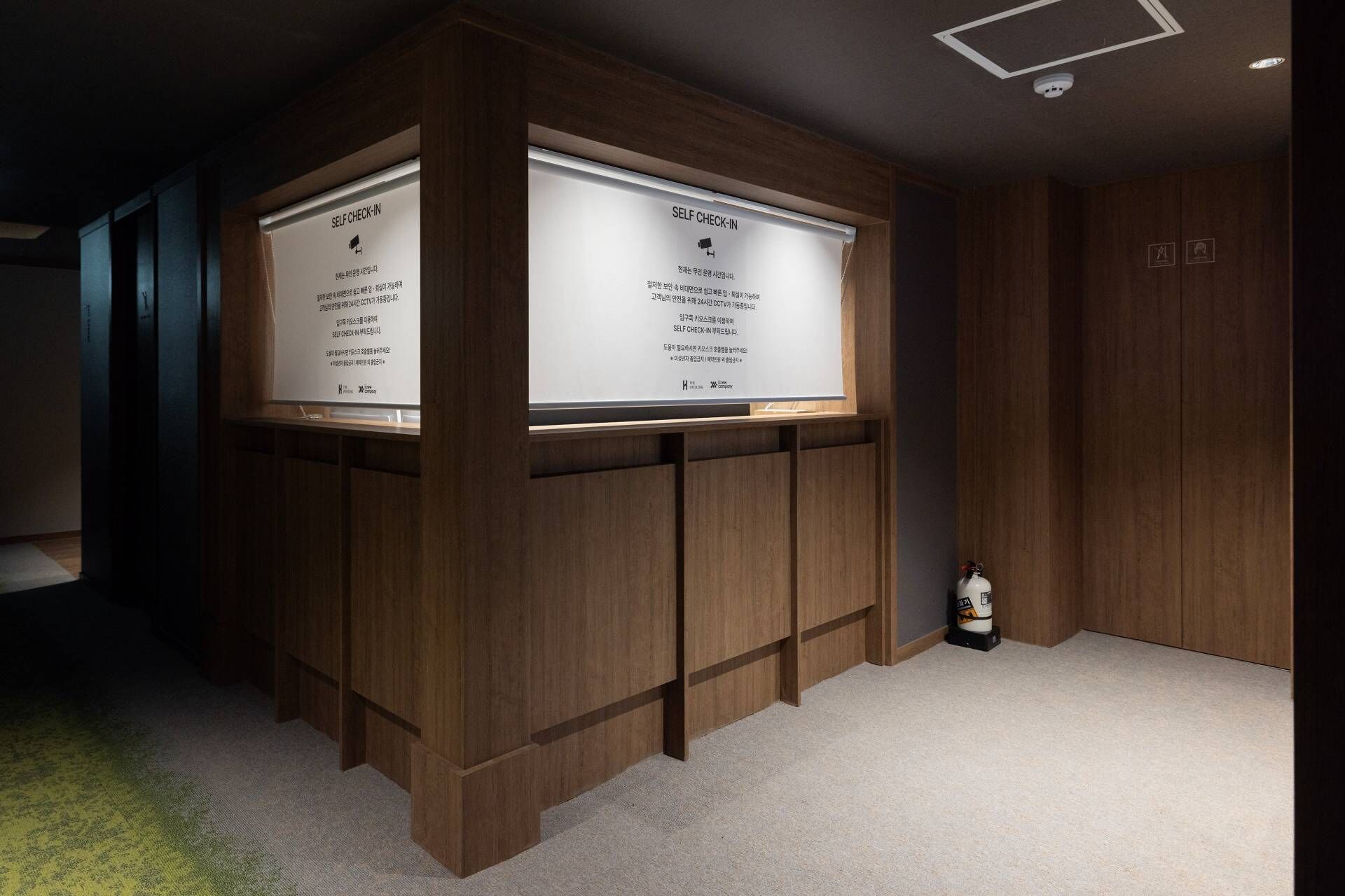 A self-check-in area with wooden paneling and a fire extinguisher on the floor.