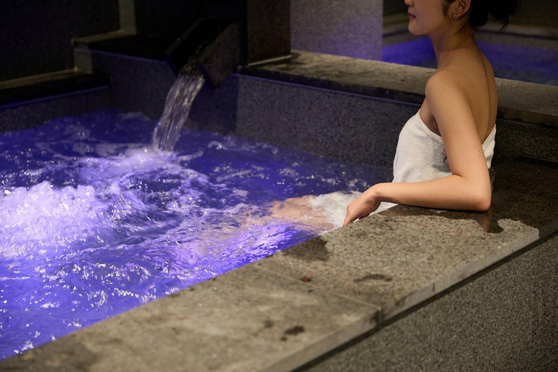 A person sitting by a pool with water flowing over the edge.