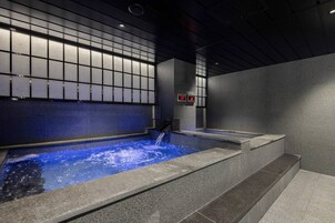 A modern indoor hot tub with a blue water feature, surrounded by stone walls and a grid-patterned ceiling.