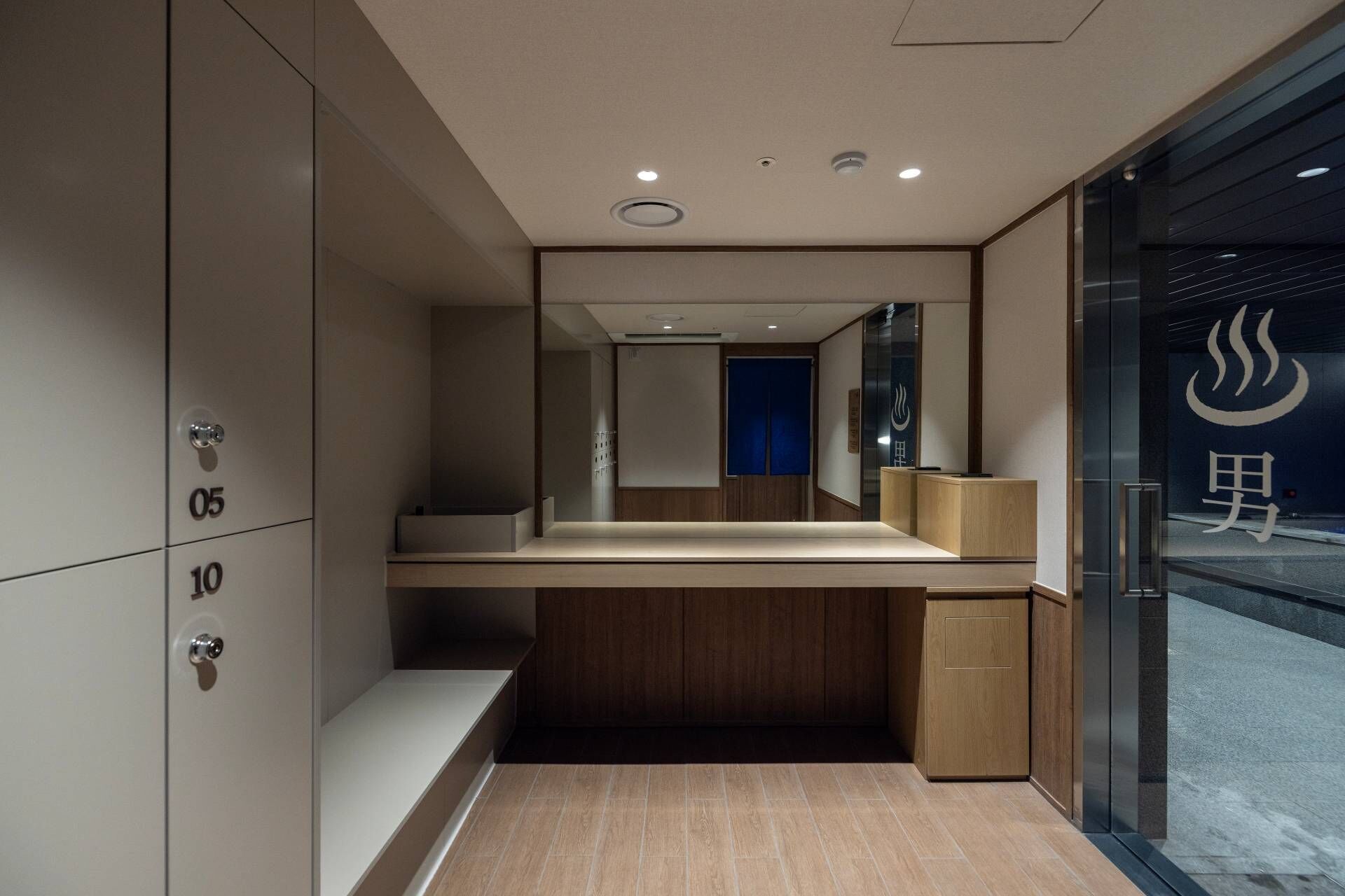 A modern hotel room with a large mirror, a wooden desk, and a small cabinet.
