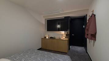 Un dormitorio pequeño y moderno con una cama, un aparador de madera, un televisor de pantalla plana y una puerta que da a otra habitación.