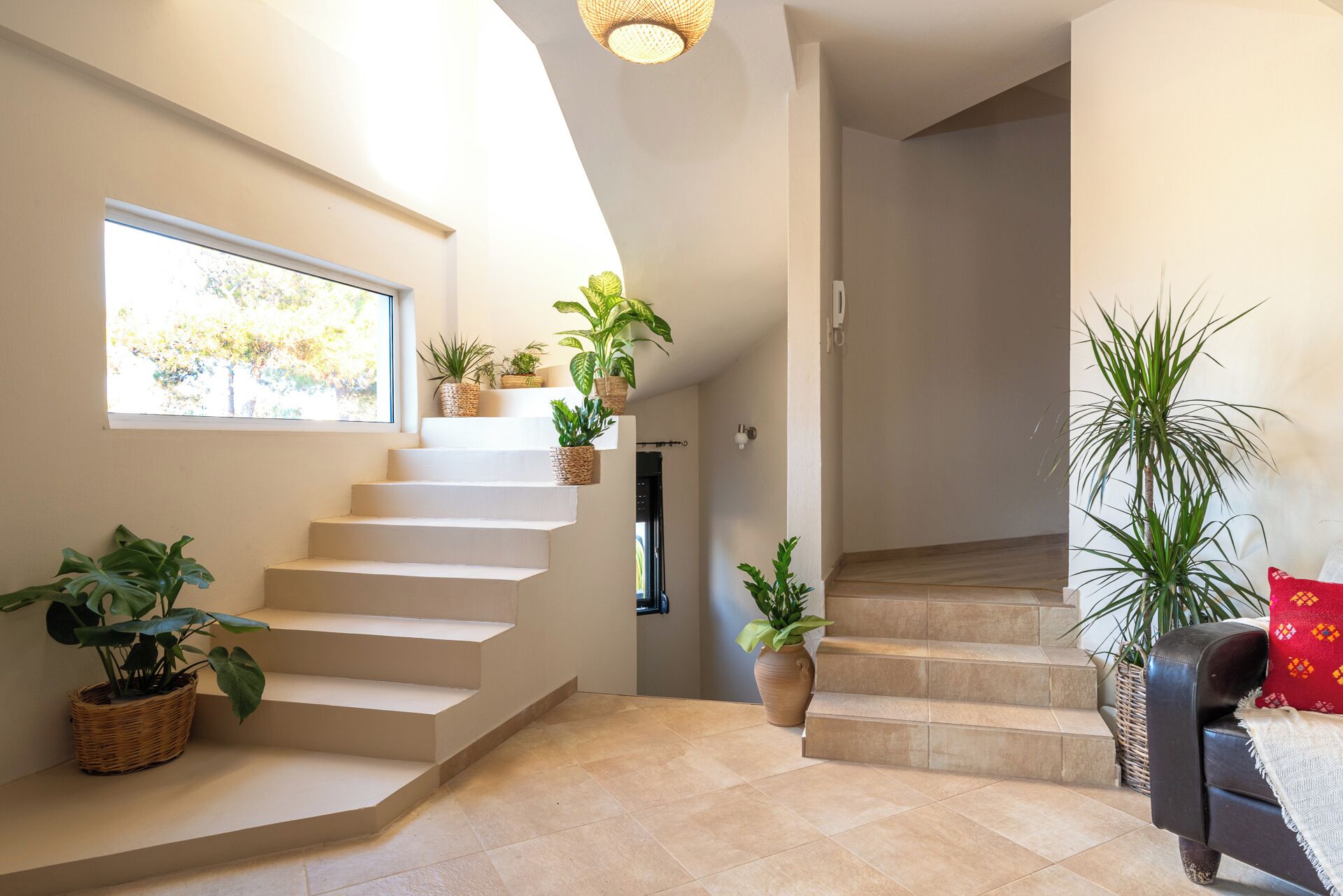 Una escala amb plantes en testos, una finestra amb vista a arbres i una porta que dona a una altra habitació.