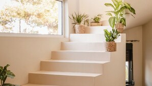 Una escalera moderna con escalones blancos, plantas en macetas y un ventanal con vista a árboles.