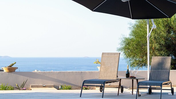 Un área junto a la piscina con dos sillones de descanso, una mesa y una sombrilla.