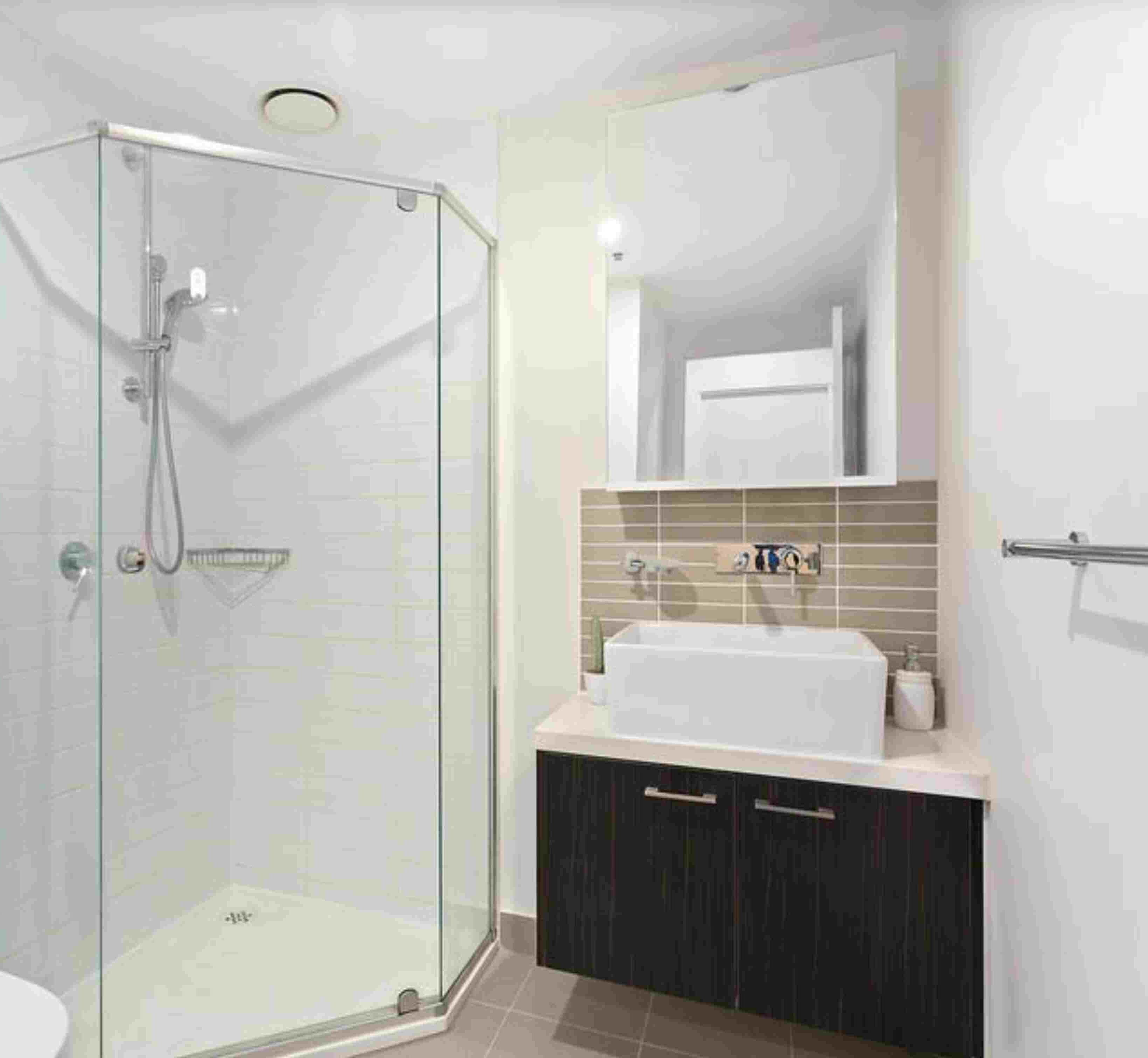 A modern bathroom with a glass shower enclosure, a sink with a mirror above, and dark cabinets.