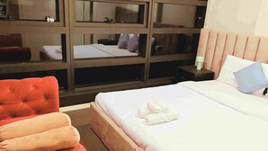 Hotellihuone, jossa on suuri sänky, kaksi punaista nojatuolia, yöpöytä ja peili.