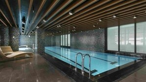 Una piscina interior moderna con un diseño largo y estrecho, rodeada de un suelo y paredes de baldosas oscuras.
