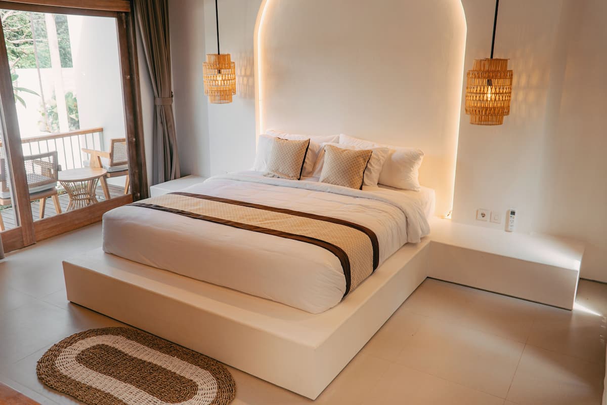 A modern bedroom with a large bed, a small seating area, and a view of the outdoors.