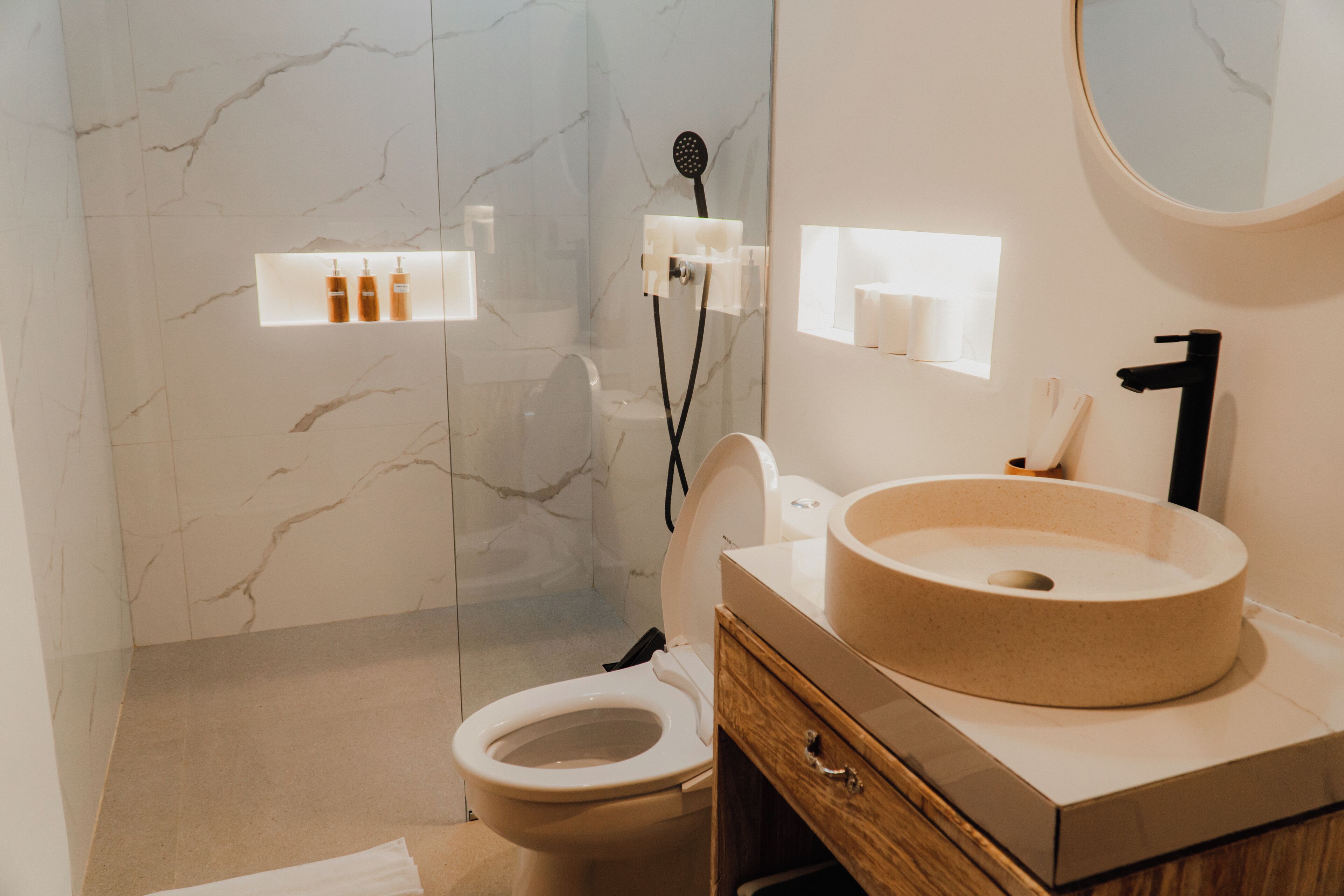 A modern bathroom with a marble wall, a round sink, and a toilet.