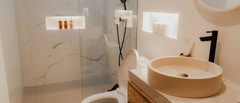 A modern bathroom with a marble wall, a round sink, and a toilet.