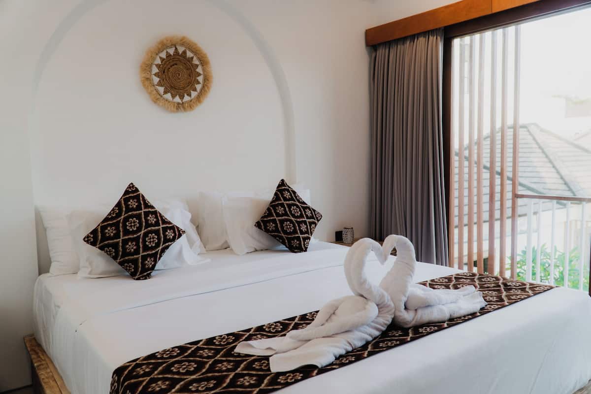 A hotel room with a bed, pillows, a towel arrangement, and a view through the window.