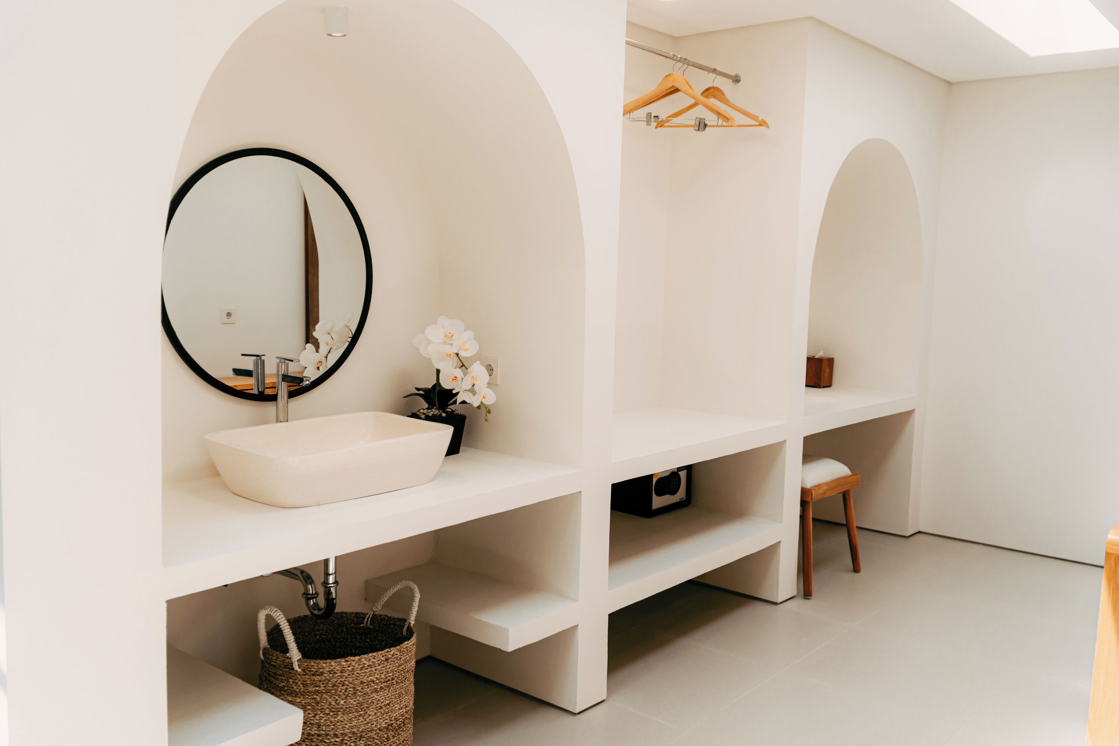 Ein modernes Badezimmer mit einem weißen Waschbecken, einem runden Spiegel und weißen Regalen.