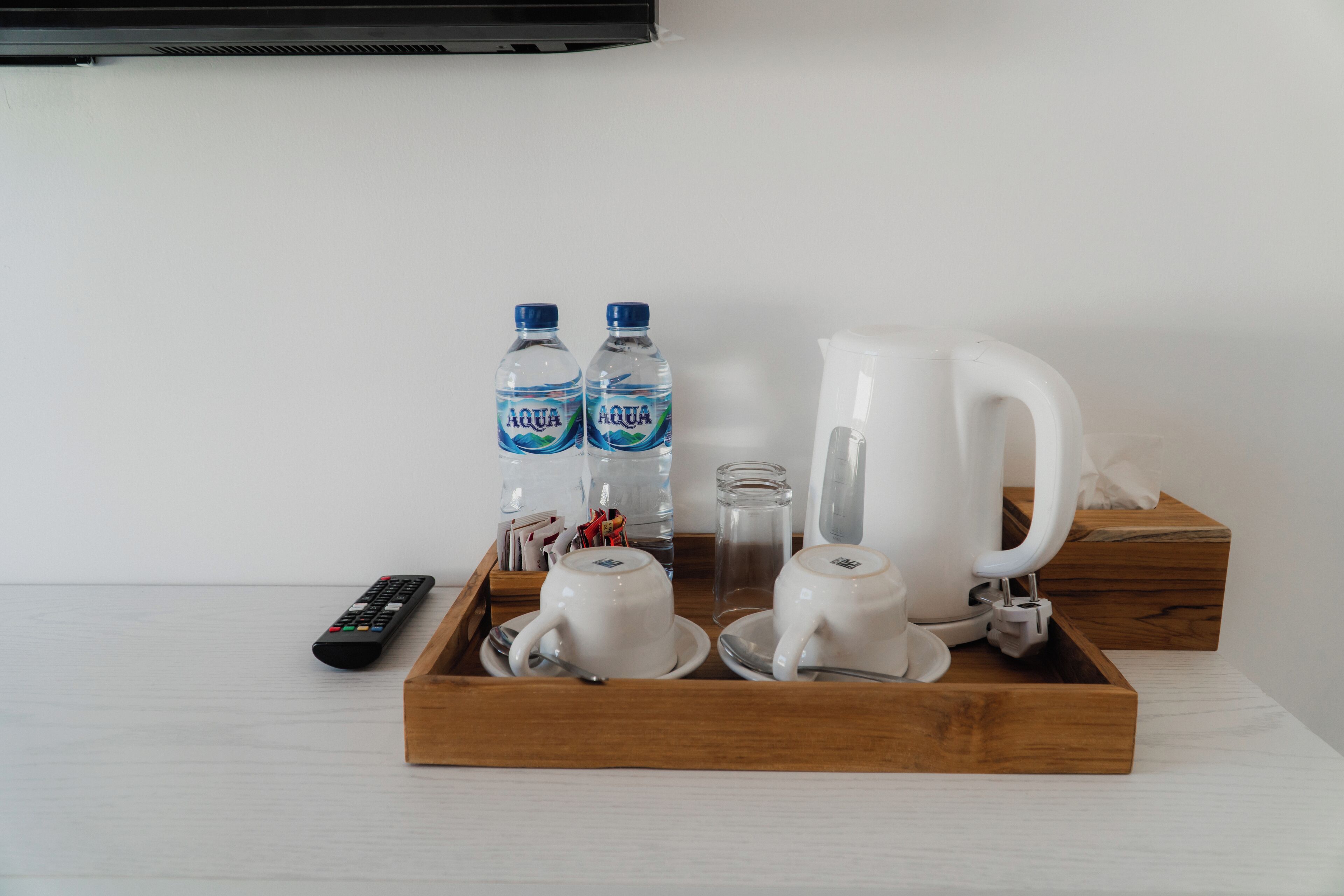 A tray with two water bottles, a white pitcher, and a remote control on a wooden surface.