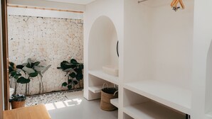 A modern bathroom with a stone wall, a white sink, and a wooden chair. - Sanjula Uluwatu (Uluwatu)