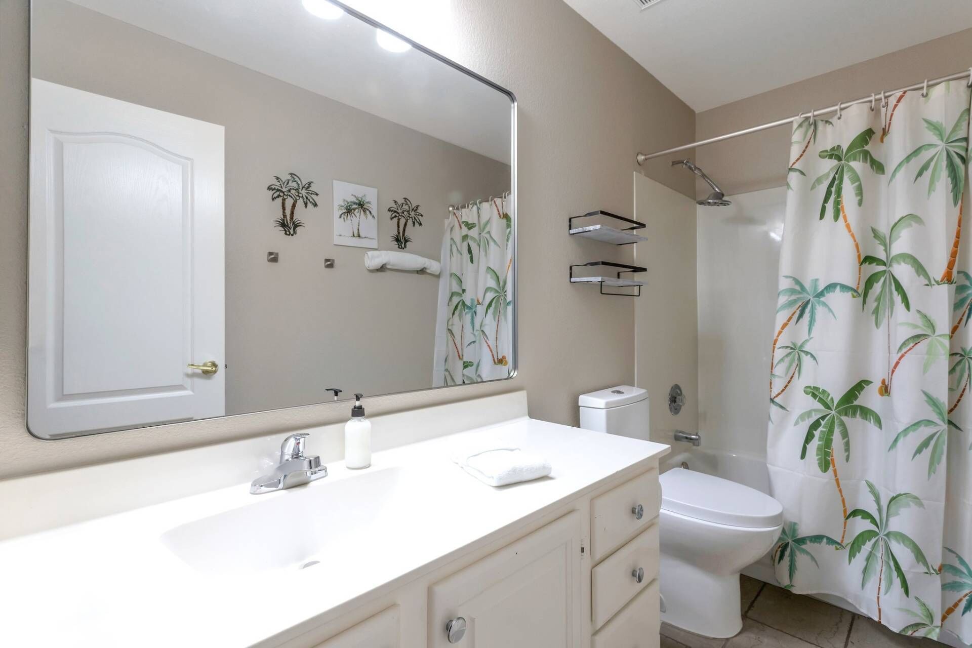 Un baño con un lavamanos blanco, un inodoro, una ducha con cortina de palmera y un espejo sobre el lavamanos.