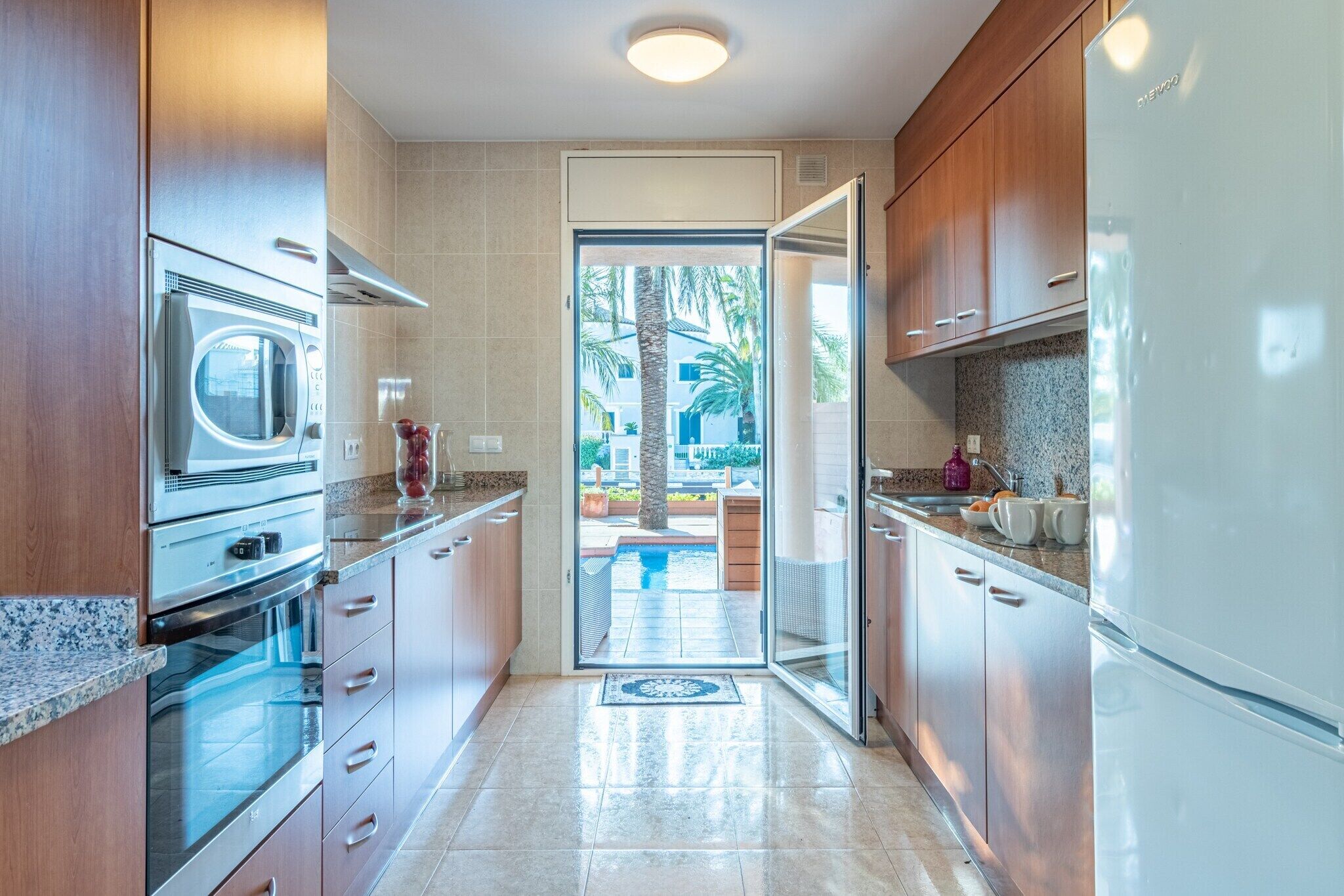 A modern kitchen with stainless steel appliances, wooden cabinets, and a view to an outdoor patio.