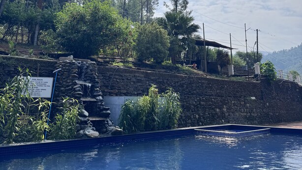 Une piscine avec un mur en pierre et une cascade décorative.