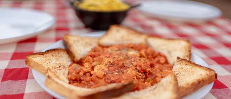 A plate of toasted bread with a tomato-based spread, a bowl of yellow food, and a white plate on a checkered tablecloth.