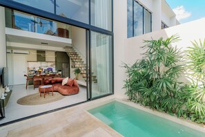 A modern house with a glass-enclosed dining area, a pool, and a staircase leading to an upper level. - The Oasis III Townhouses By Breig (Canggu)