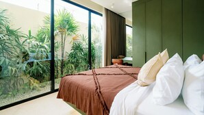 Ein Schlafzimmer mit einem großen Bett, einem grünen Kleiderschrank und Blick auf einen Garten durch eine Glastür.