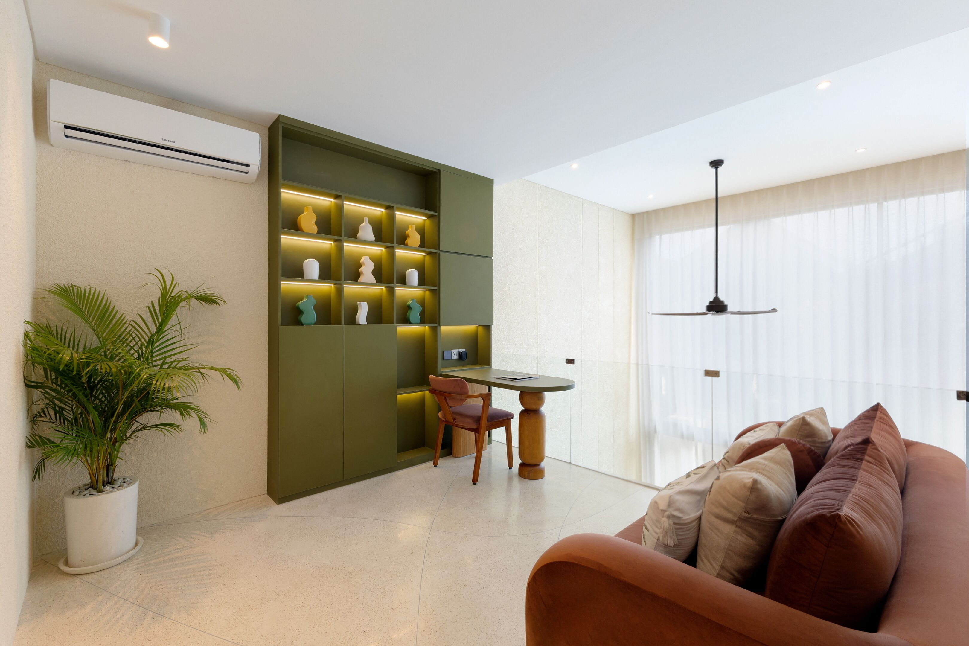 A modern living room with a sofa, a dining table, and a green shelving unit with decorative items.