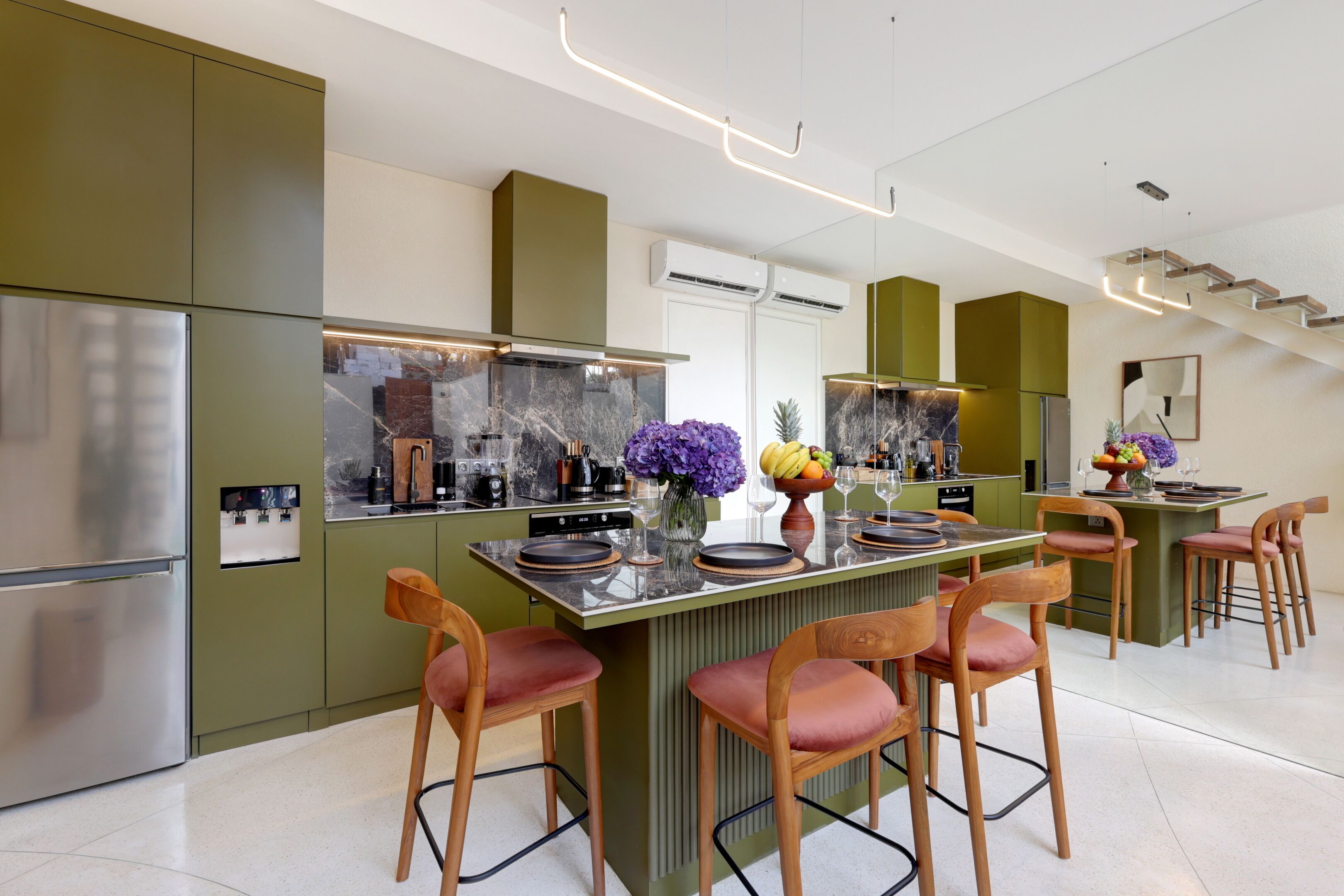 A modern kitchen with a central island, bar stools, and a staircase leading to an upper level.