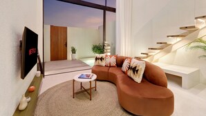 Ein modernes Wohnzimmer mit einer gebogenen Couch, einem kleinen runden Tisch und einem an der Wand montierten Fernseher.