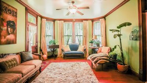 A cozy room with a vintage sofa, a blue armchair, a red carpet, and a ceiling fan.