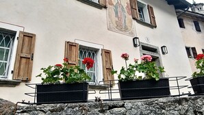 Un edificio con contraventanas de madera, un mural y plantas en macetas.