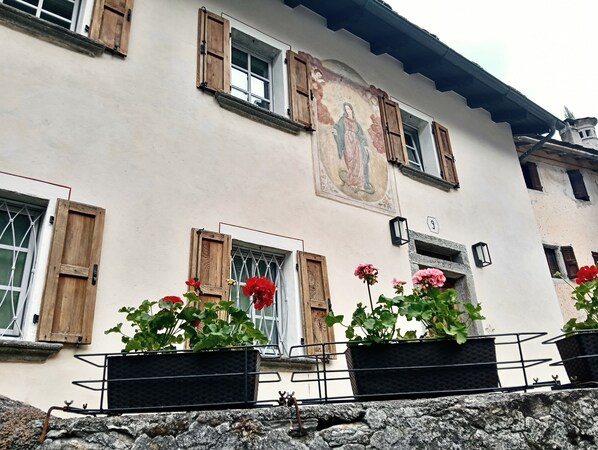 Um edifício com venezianas de madeira, um mural e plantas em vasos.