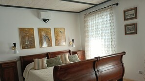 Un dormitorio con cama de madera, ropa de cama blanca, dos lámparas fijadas a la pared y tres cuadros enmarcados.