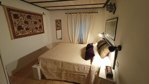 Une chambre à coucher avec un lit, une table de chevet, une lampe et une fenêtre avec des rideaux.