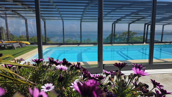 A pool area with a view of the ocean, surrounded by a covered patio with chairs.