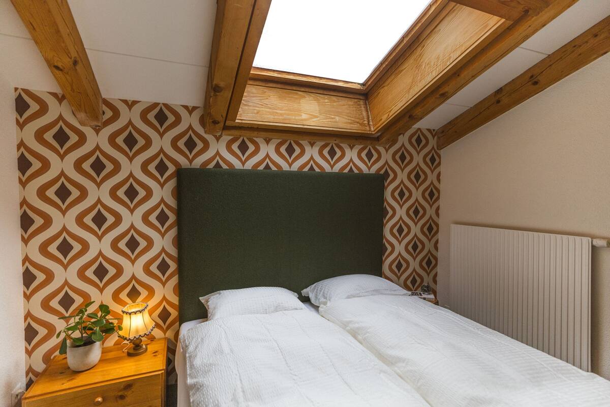 Ein Schlafzimmer mit Oberlichter, strukturiertem Wandpapier, einem Nachttisch mit Lampe und einer Heizung.