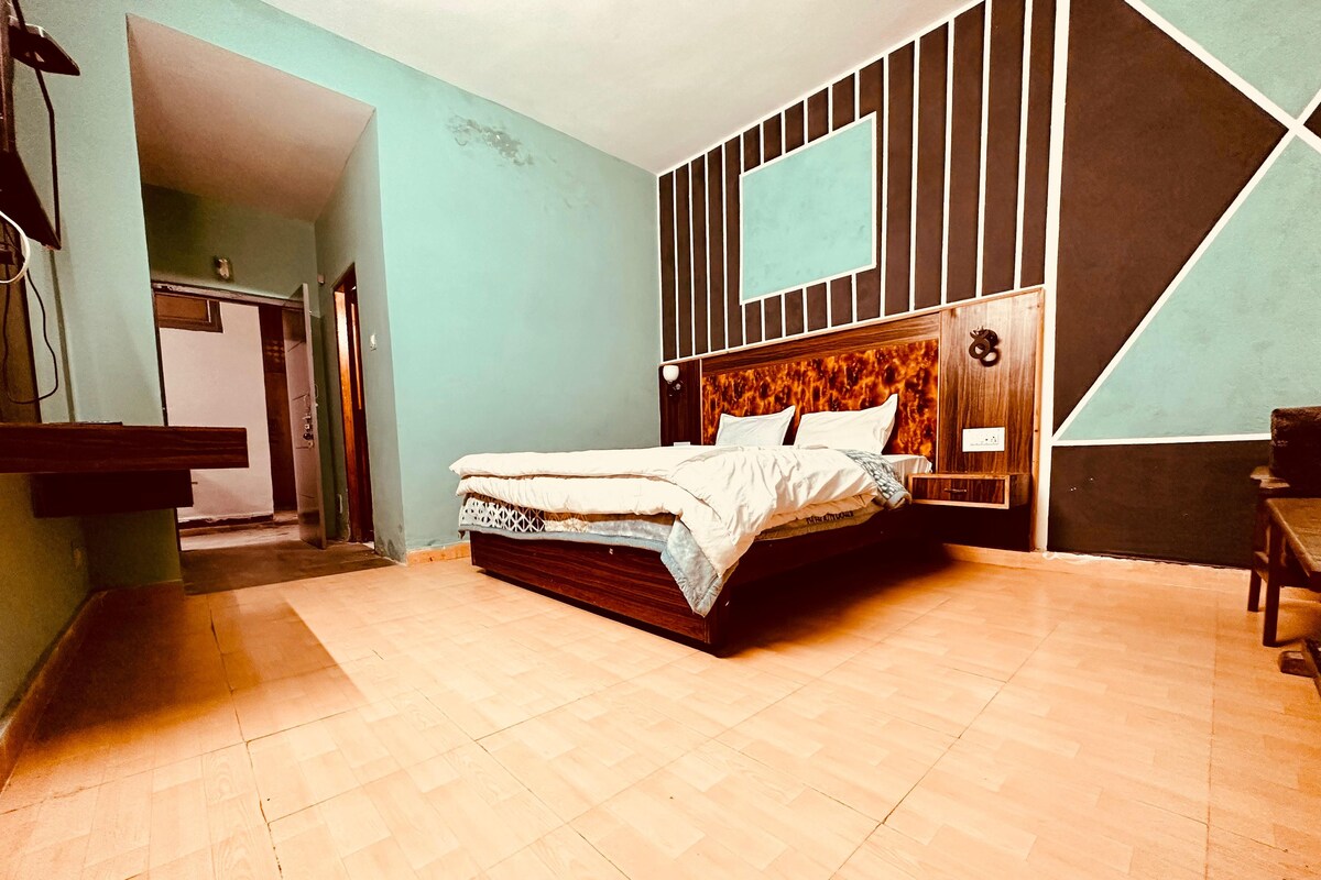 A bedroom with a wooden bed, a nightstand, a wall-mounted TV, and a door leading to another room.