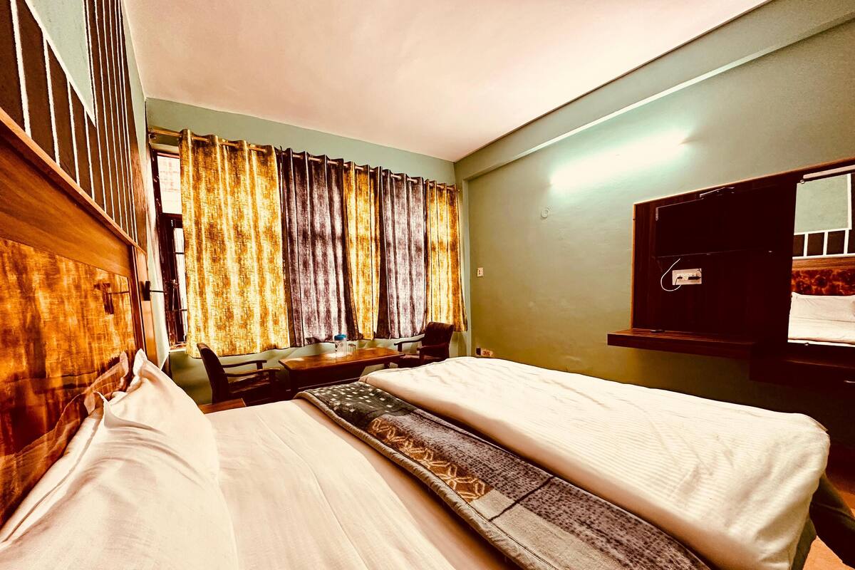 A hotel room with two beds, a desk, a chair, and a window with curtains.