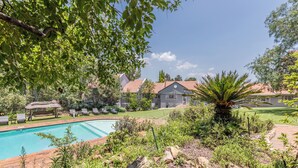 A pool surrounded by lush greenery, a gazebo, and a building with a red roof. - Grand Manor  (Muldersdrift)
