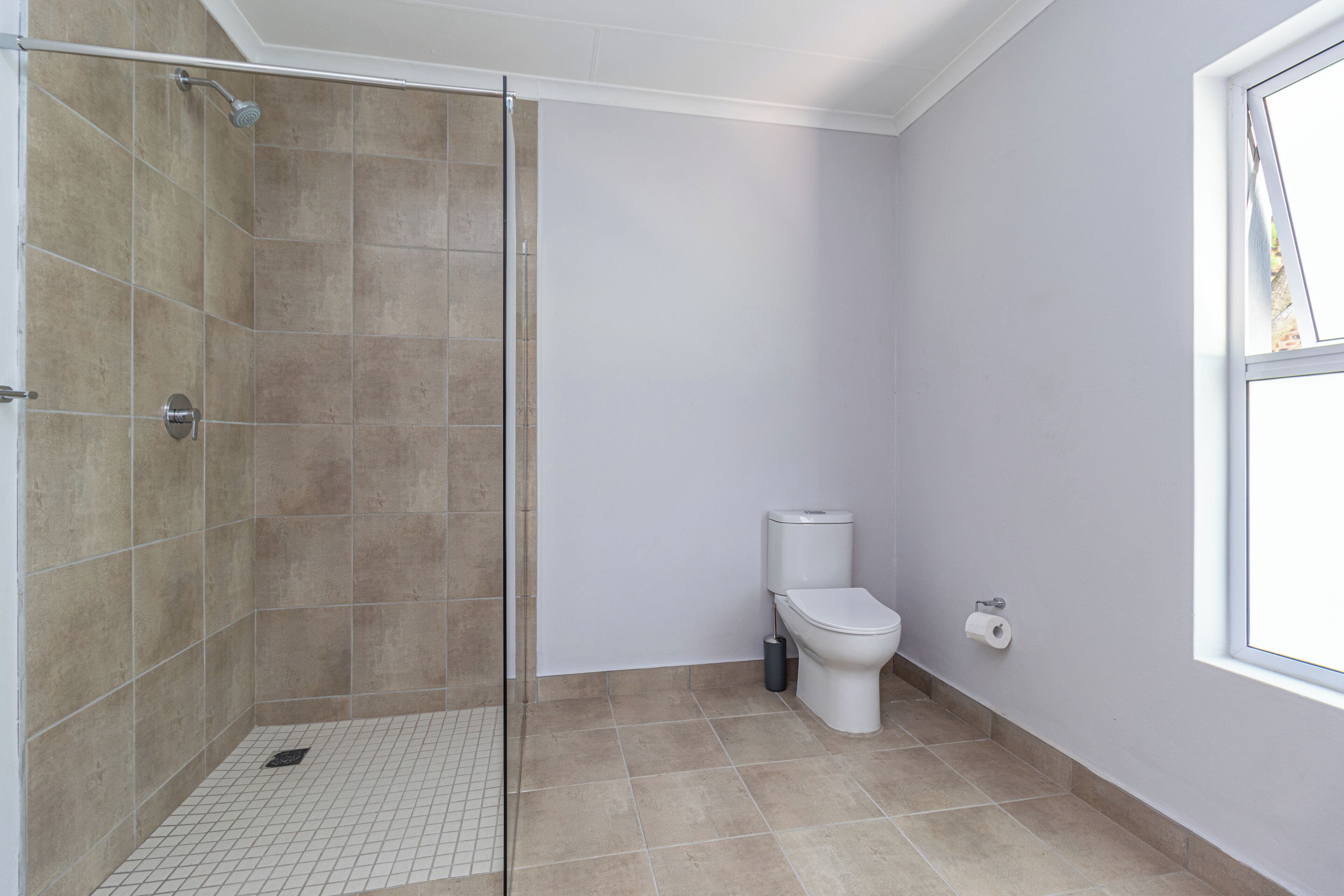 A bathroom with a shower, toilet, and a window.