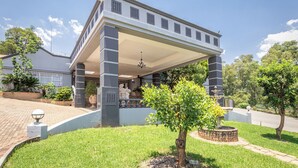 A large, two-story building with a covered porch supported by columns, surrounded by well-maintained lawns and trees. - Grand Manor  (Muldersdrift)