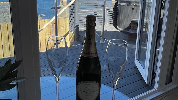 En balkon med en champagneflaske og to glas på et bord, med udsigt over kysten.