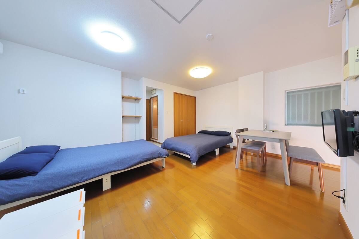 Una habitación tipo dormitorio con dos camas individuales, un escritorio, una silla, un televisor y un armario.