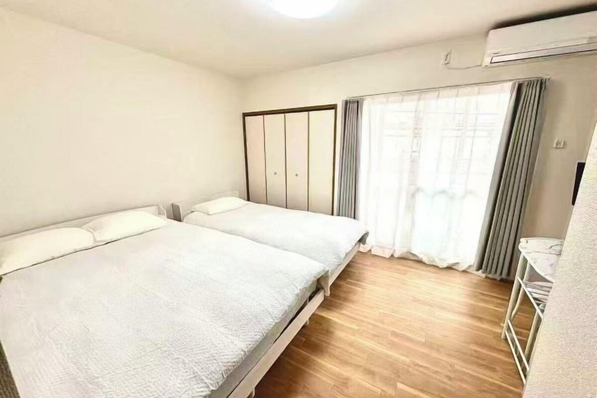 Una habitación de hotel con dos camas, un armario, una mesita y una ventana con cortinas.