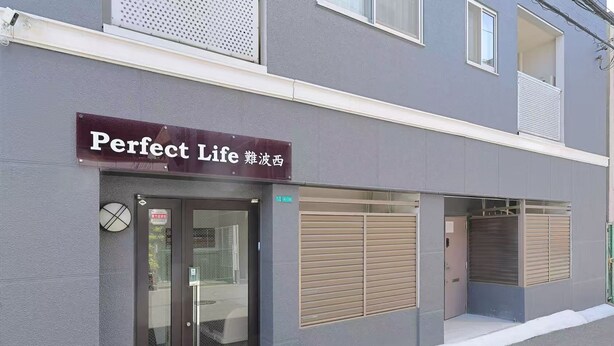 Un edificio con un letrero que dice "Perfect Life" y una puerta con persiana cerrada.