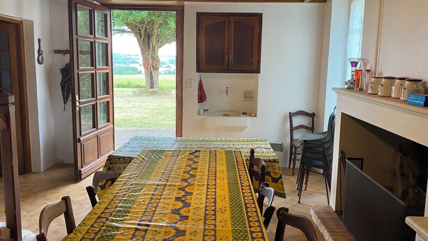 Comedor con mesa dispuesta para seis personas, techo de madera, chimenea y vista a un árbol a través de una puerta abierta.