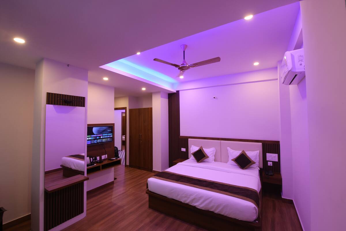 Una camera d'albergo moderna con un letto grande, una ventola a soffitto, illuminazione incassata, una televisione e un pavimento in legno.
