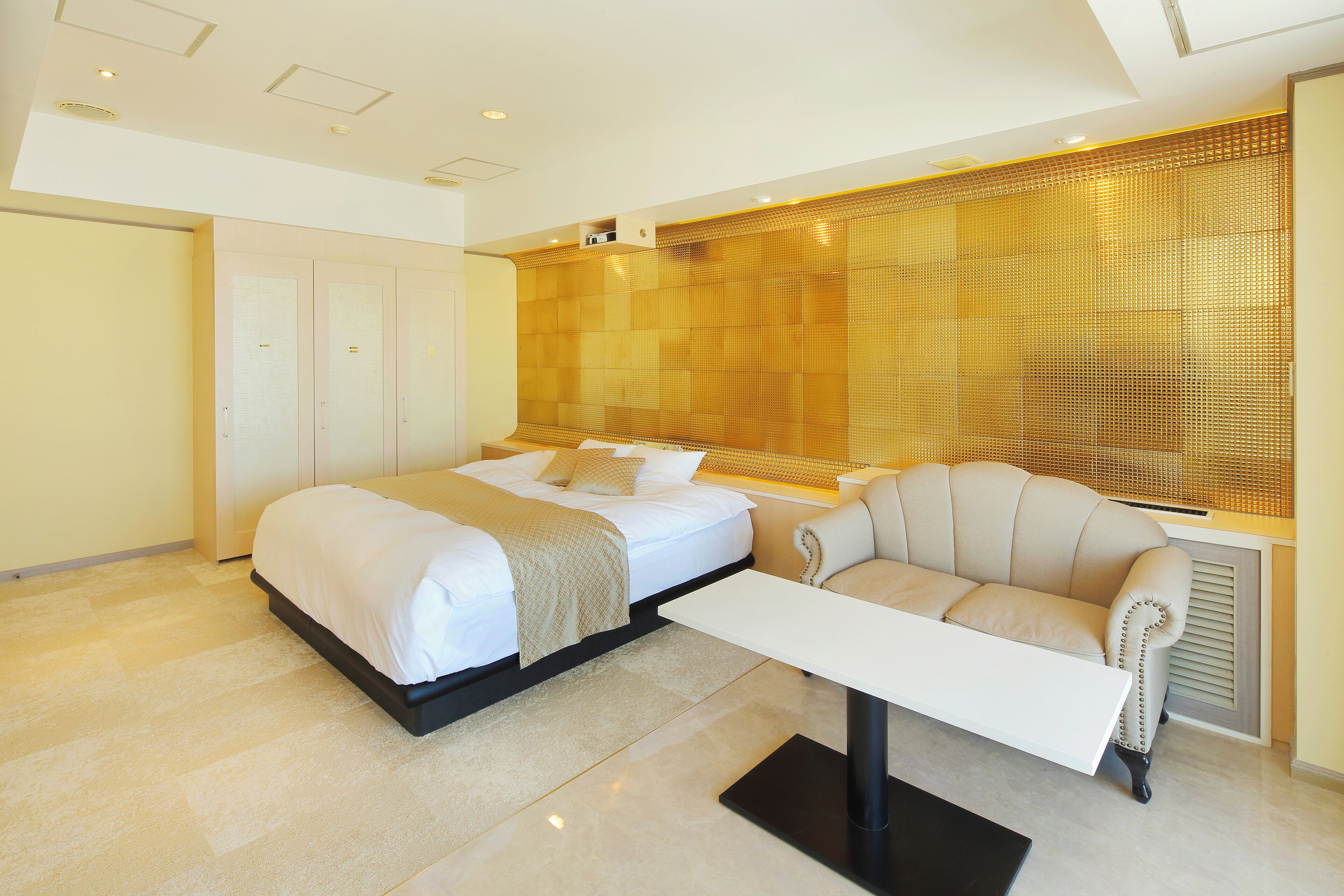 A modern hotel room with a large bed, a sofa, and a dining table.