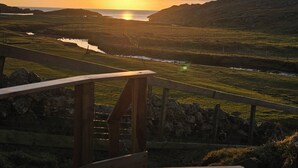 A wooden deck with a view of a sunset over a hilly landscape. - Oldshoremore Croft Cabins (Oldshore)