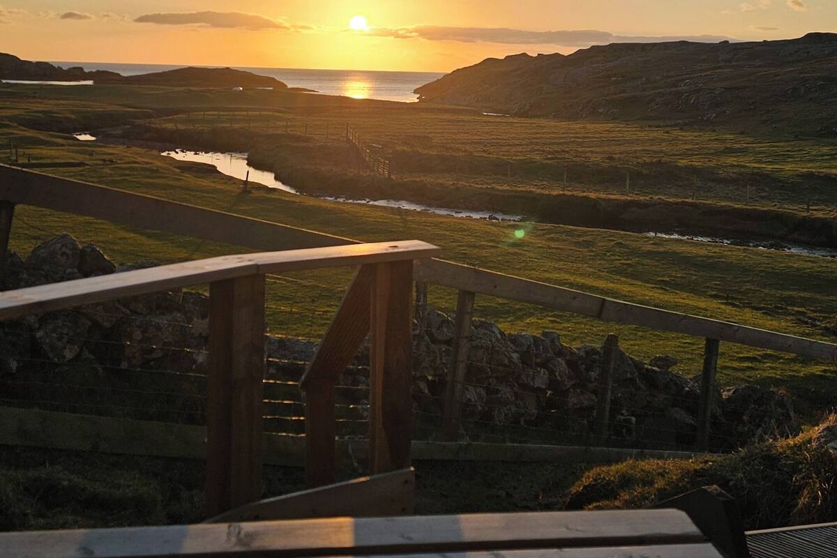 A wooden deck with a view of a sunset over a hilly landscape.