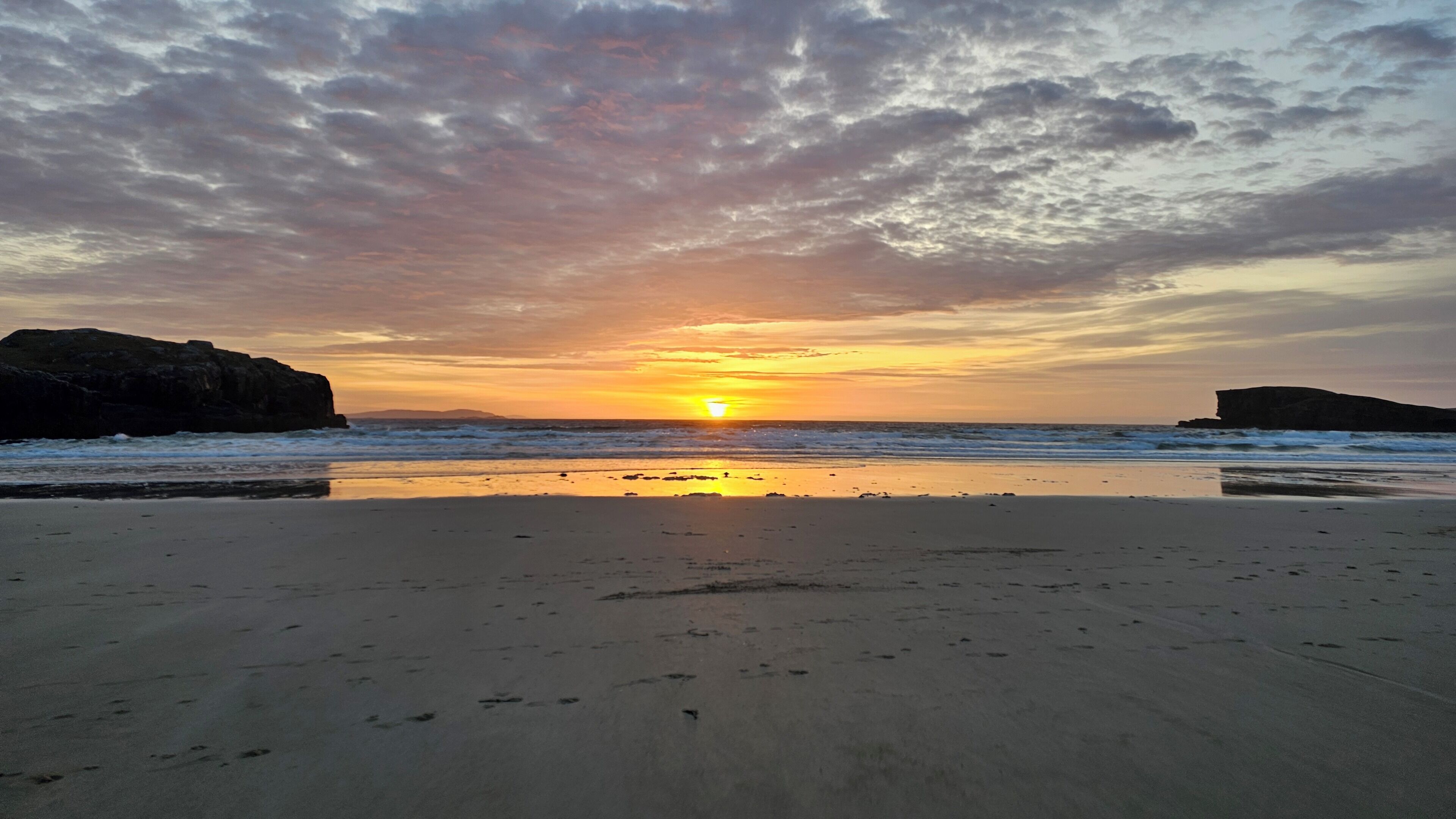Una playa con atardecer, formaciones rocosas y olas tranquilas.