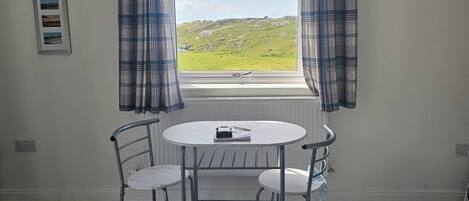 A room with a window, a table with chairs, a clock on the wall, and a framed photo.